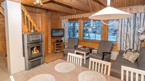 A cozy cabin interior with a fireplace, wooden walls, a TV, and a seating area with a table and chairs.