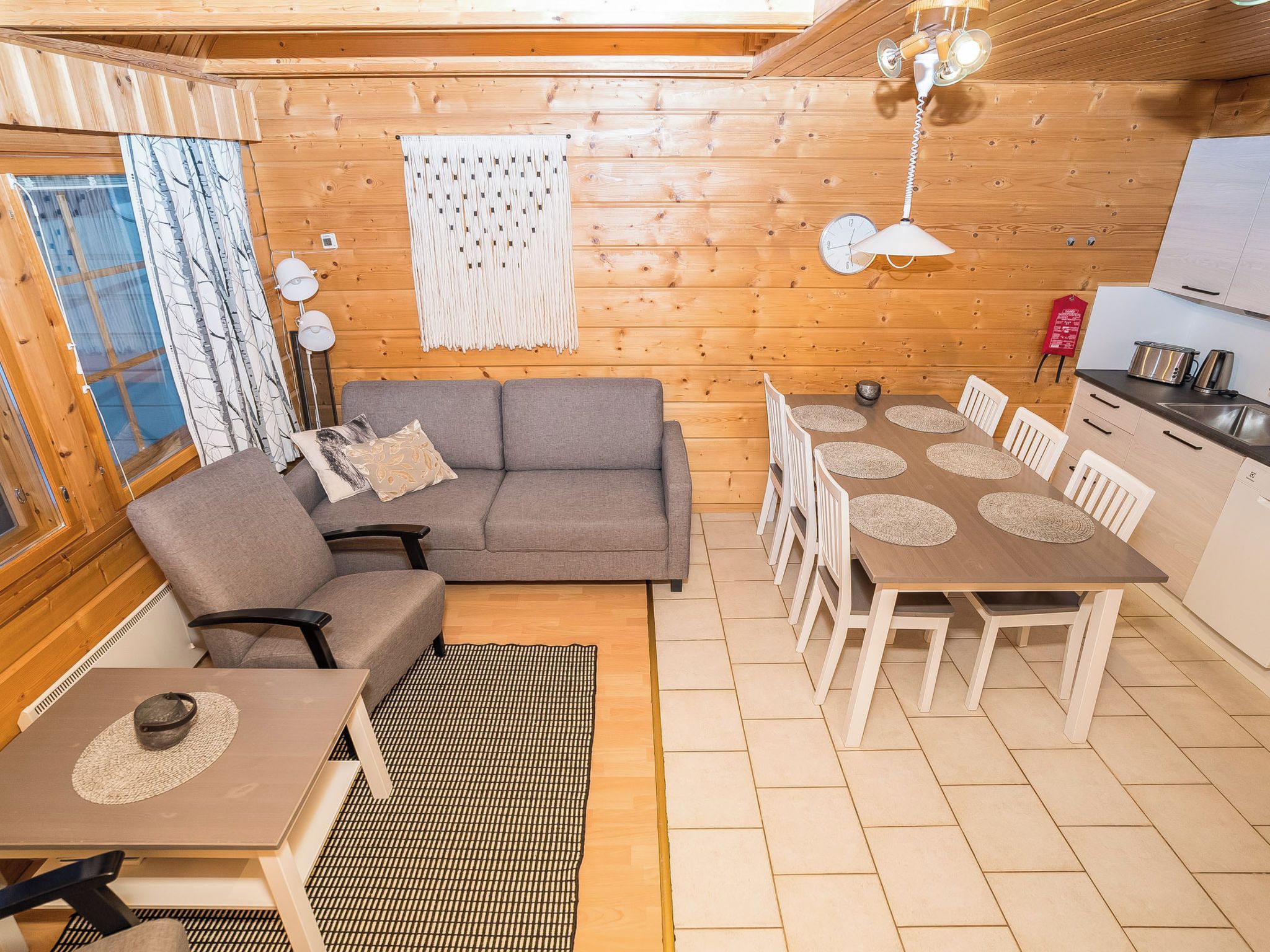 Un interior acogedor con sofá, mesa de comedor, sillas, paredes de madera y una zona de cocina.