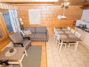 A cozy interior with a sofa, dining table, and chairs, wooden walls, and a kitchen area.