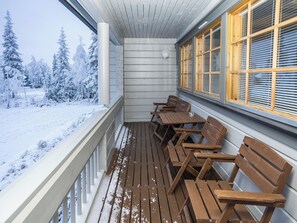 Una terraza de madera con bancos y una mesa, con vista a un paisaje nevado con árboles.