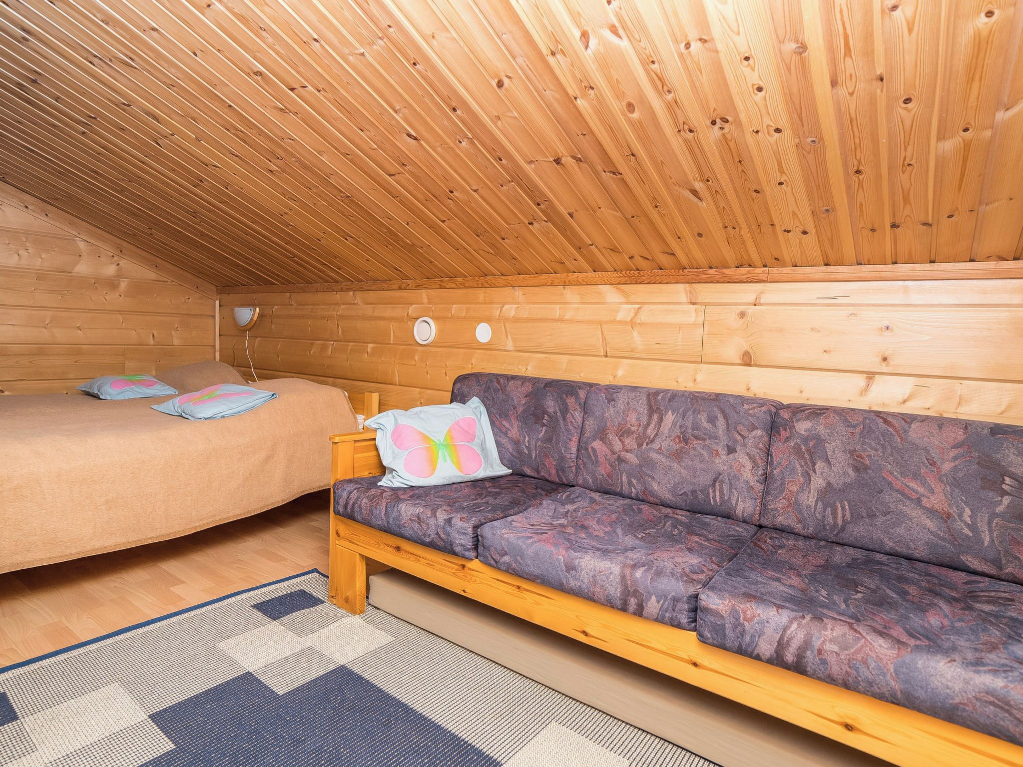 Een gezellig chaletinterieur met een houten plafond, een bed, een bank en een kamerbreed tapijt.