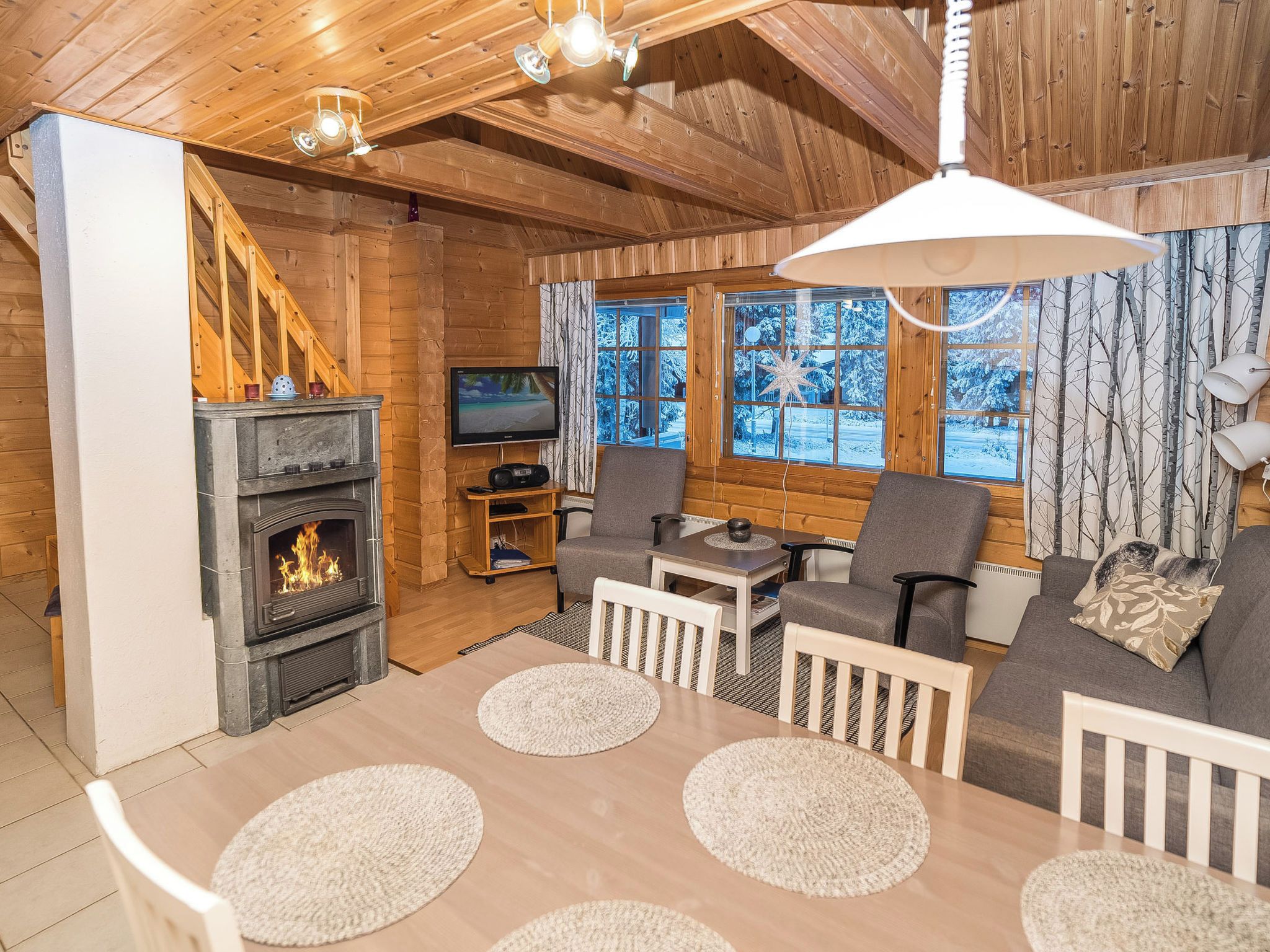 Un intérieur de chalet chaleureux avec une cheminée, des murs en bois, un téléviseur et un ensemble de canapés.