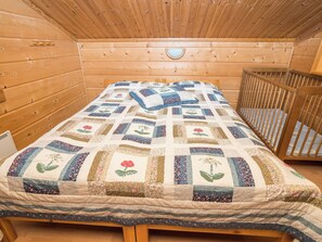 A wooden cabin room with a bed, a crib, and a wooden ceiling.