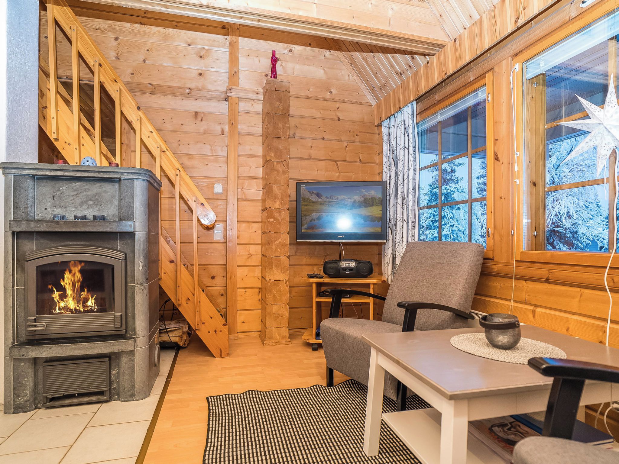 A cozy cabin interior with a fireplace, a television, and a wooden staircase.