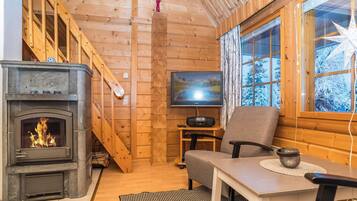 A cozy cabin interior with a fireplace, a television, and a wooden staircase.