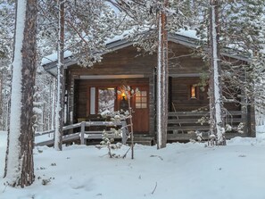 Een houten blokhut met een overdekte veranda en een open haard, omgeven door met sneeuw bedekte bomen.