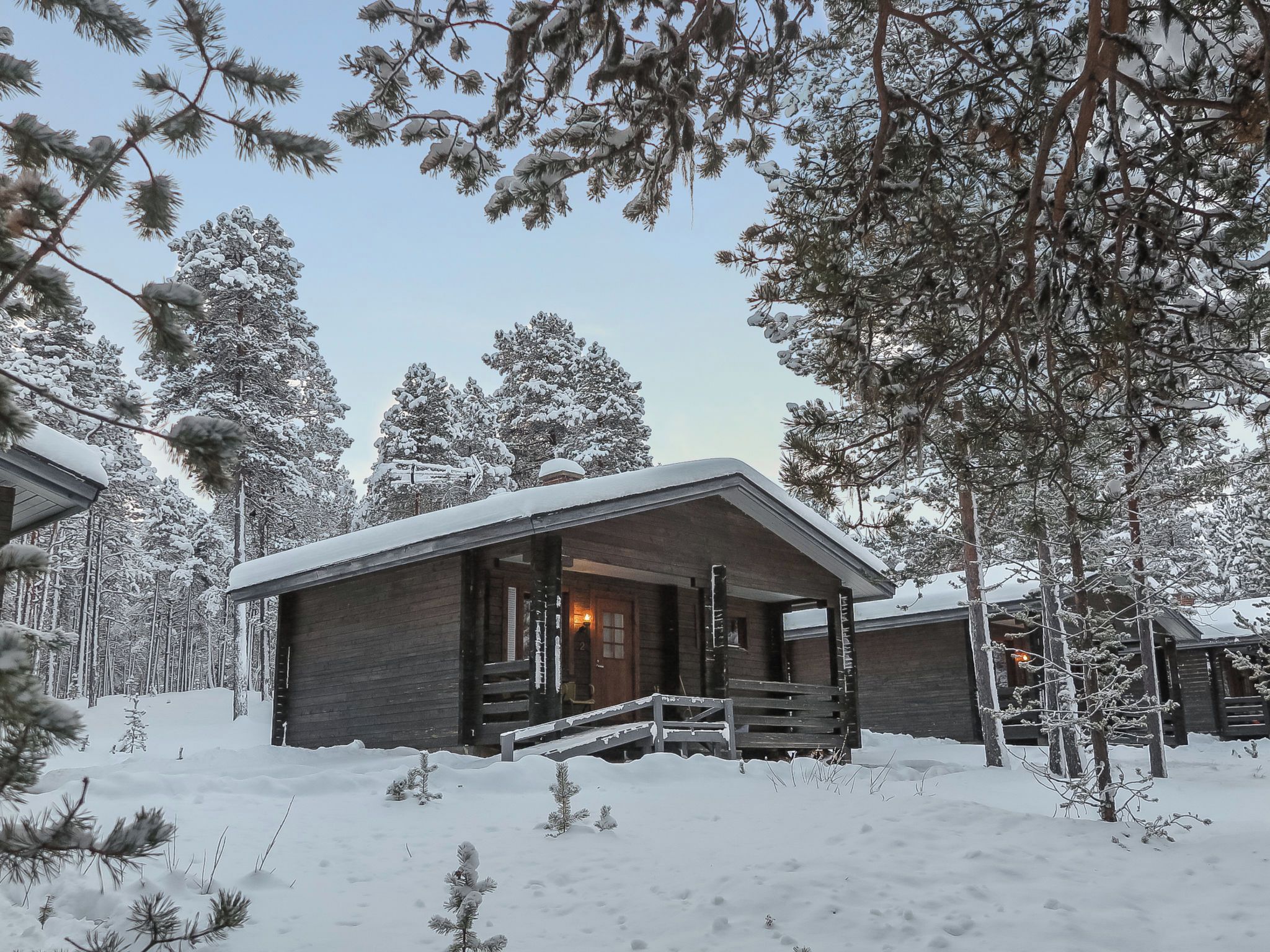 A wooden cabin with a porch and a door, surrounded by snow-covered trees.
