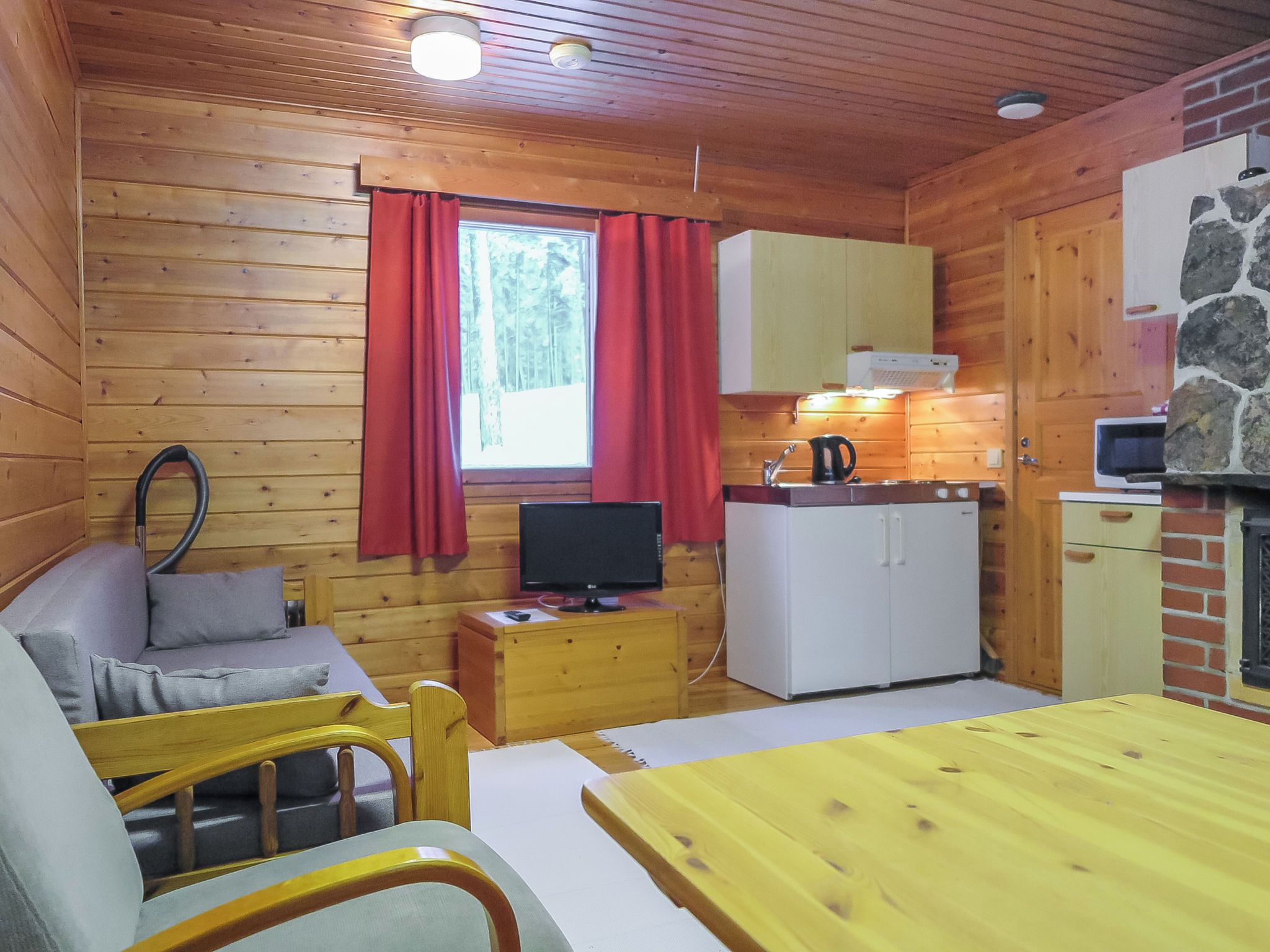A wooden cabin interior with a sofa, television, kitchenette, and a stone fireplace.