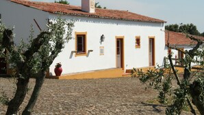 A white building with a red-tiled roof, a chimney, and a cobblestone ground.