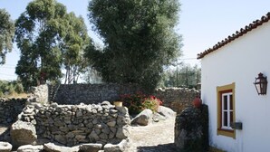 A stone wall, a white building with a yellow trim, and a garden with red flowers.