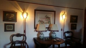 A room with two wooden chairs, a small table with a vase and a lamp, and wall-mounted lamps.