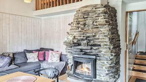 A cozy living room with a stone fireplace, a sofa with cushions, a wooden table, and a staircase. - Riekonraito a1 by Interhome (Inari)