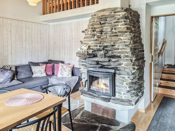 A cozy living room with a stone fireplace, a sofa with cushions, a wooden table, and a staircase.