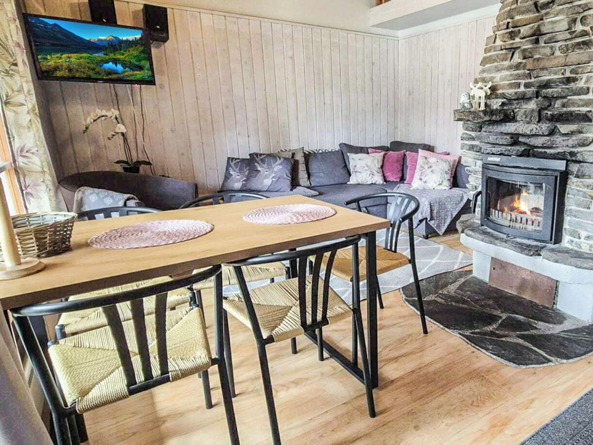 Una sala de estar acogedora con chimenea de piedra, una mesa de comedor de madera con sillas, un sofá con cojines y un televisor montado en la pared.