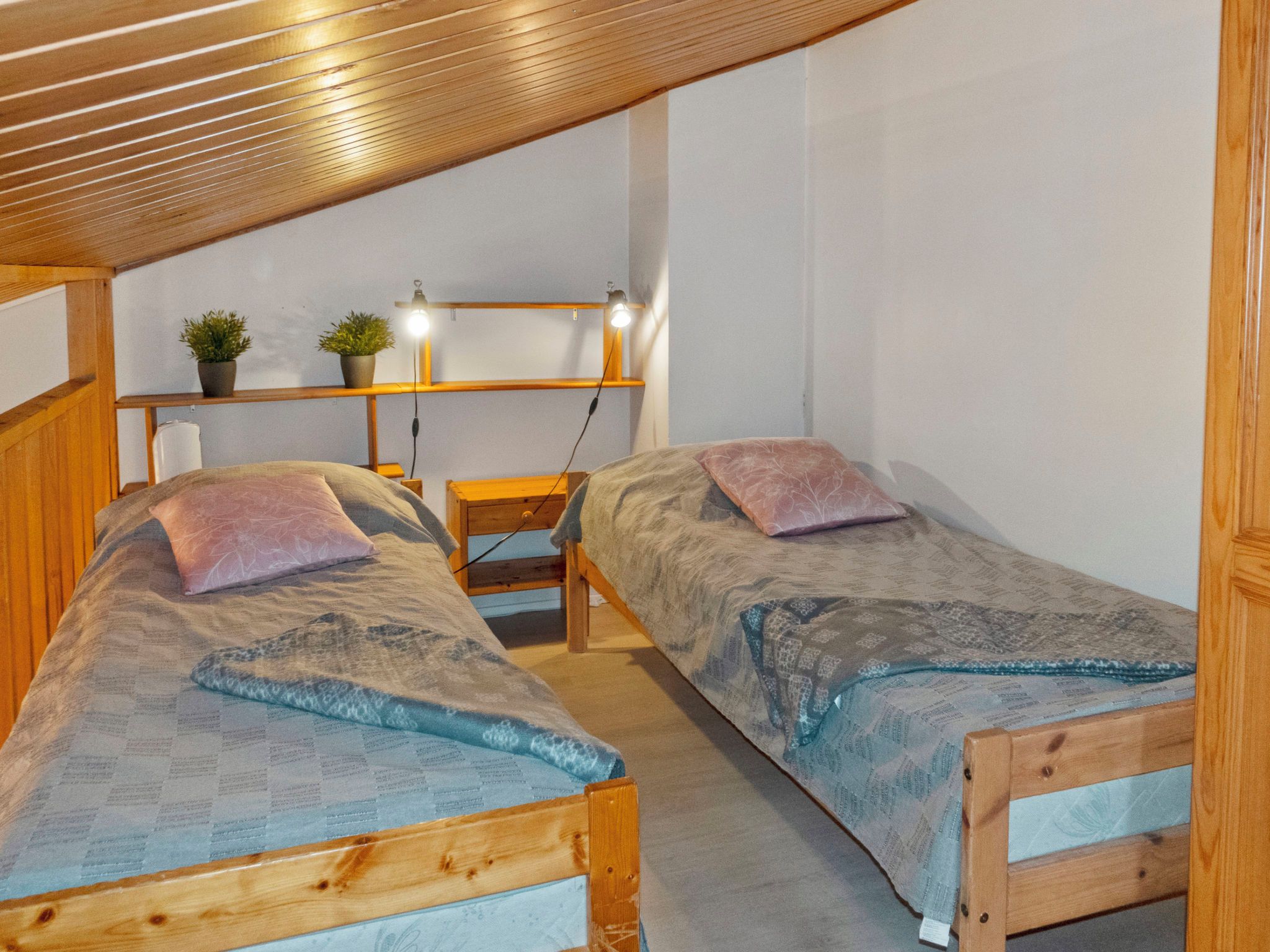 A small, cozy room with two wooden beds, a desk, and a shelf with plants.