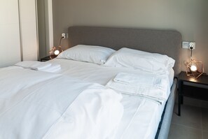 A neatly made bed with white linens, a headboard, and bedside lamps.