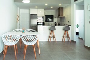 A modern kitchen with white cabinetry, a central island with stools, and a dining table with white chairs.
