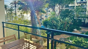 A balcony with a wooden table and chairs, overlooking a lush garden with palm trees and a building complex in the background. - Skol Apartments Marbella beachfront, central with views and WIFI - 2 bedrooms (Marbella)