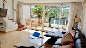 A modern living room with a sofa, a coffee table, and a TV mounted on the wall. There is a balcony with a table and chairs, and a staircase leading to an upper floor. - Skol Apartments Marbella beachfront, central with views and WIFI - 2 bedrooms (Marbella)