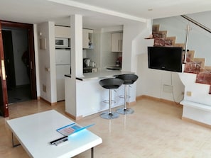 A modern kitchen with white cabinets, a microwave, and a coffee machine. There are two black bar stools and a flat-screen TV mounted on the wall. - Skol Apartments Marbella beachfront, central with views and WIFI - 2 bedrooms (Marbella)