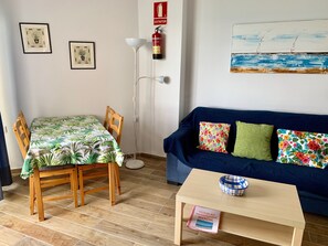 A room with a dining table, chairs, a sofa, a floor lamp, and a painting on the wall. - Skol Apartments Marbella Beachfront Central Studios with views (Marbella)