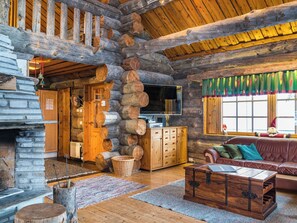 Ein rustikales Blockhaus-Interieur mit Kamin aus Stein, Holzschränken, einem Ledersofa und einem Fernseher.