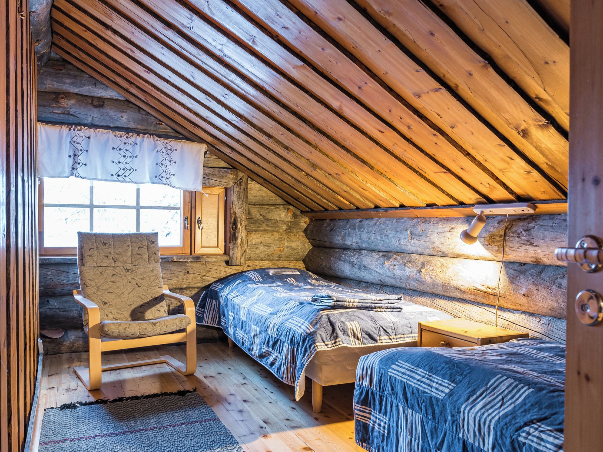 A cozy cabin with a loft bedroom, a wooden chair, and a window with curtains.