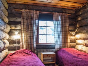 A cabin room with two beds, a window with plaid curtains, and a small bedside table.