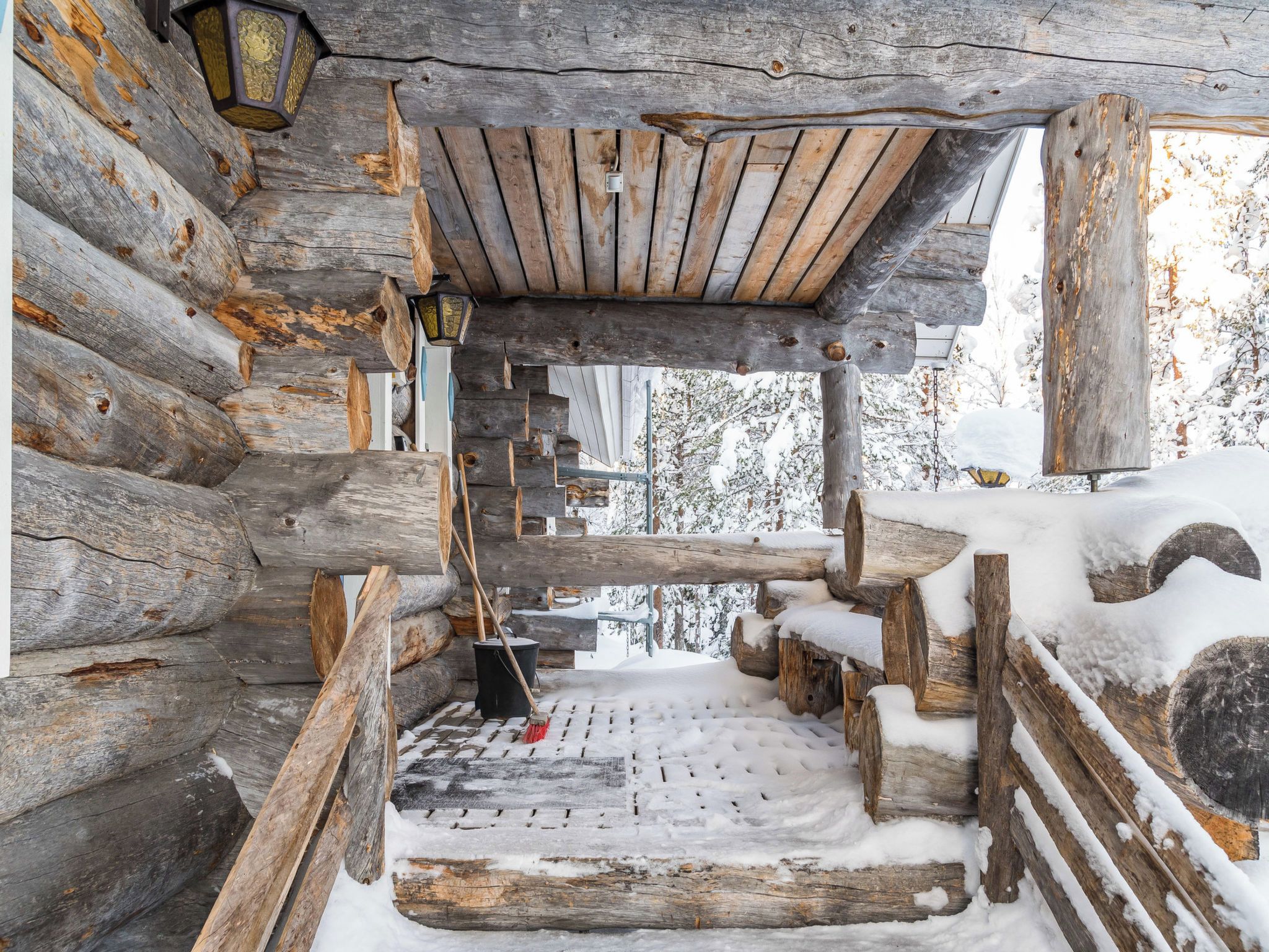 A log cabin interior with a snow-covered wooden floor and a rustic wooden ceiling.