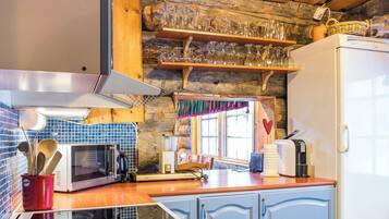 A kitchen with a microwave, toaster, and refrigerator. There is a wooden shelf with glassware above the counter.