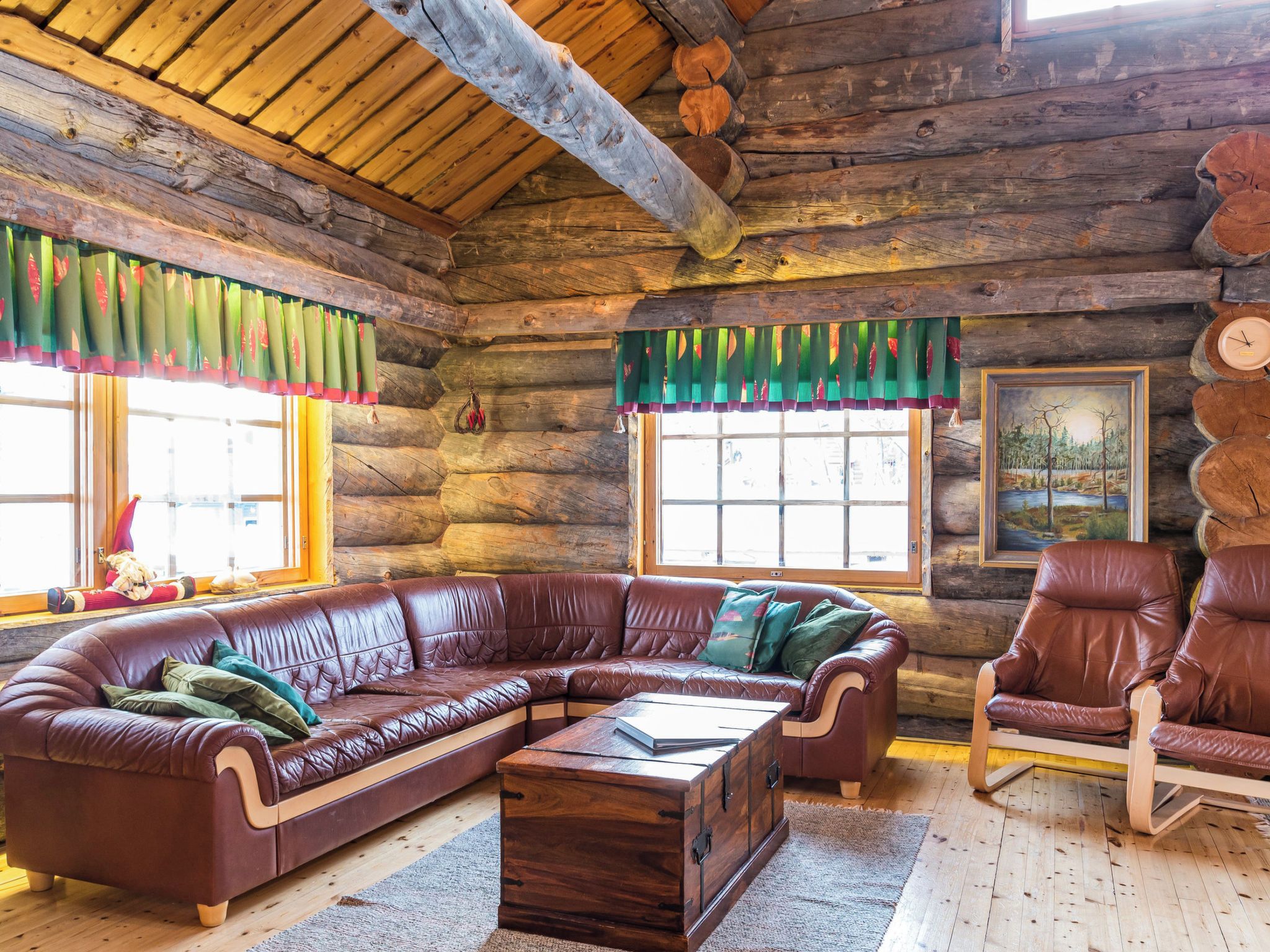 A log cabin interior with a leather sectional sofa, a wooden coffee table, and leather armchairs.