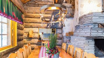A rustic wooden interior with a dining table set for four, a fireplace, and a hanging light fixture.