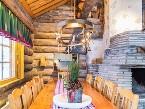 A rustic wooden interior with a dining table set for four, a fireplace, and a hanging light fixture. - Terakka by Interhome (Kittilä)