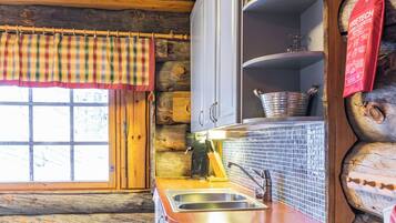 A rustic kitchen with wooden walls, a window with plaid curtains, a sink, and a stove.