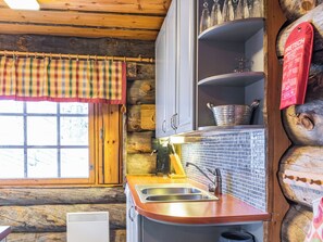 A rustic kitchen with wooden walls, a window with plaid curtains, a sink, and a stove.