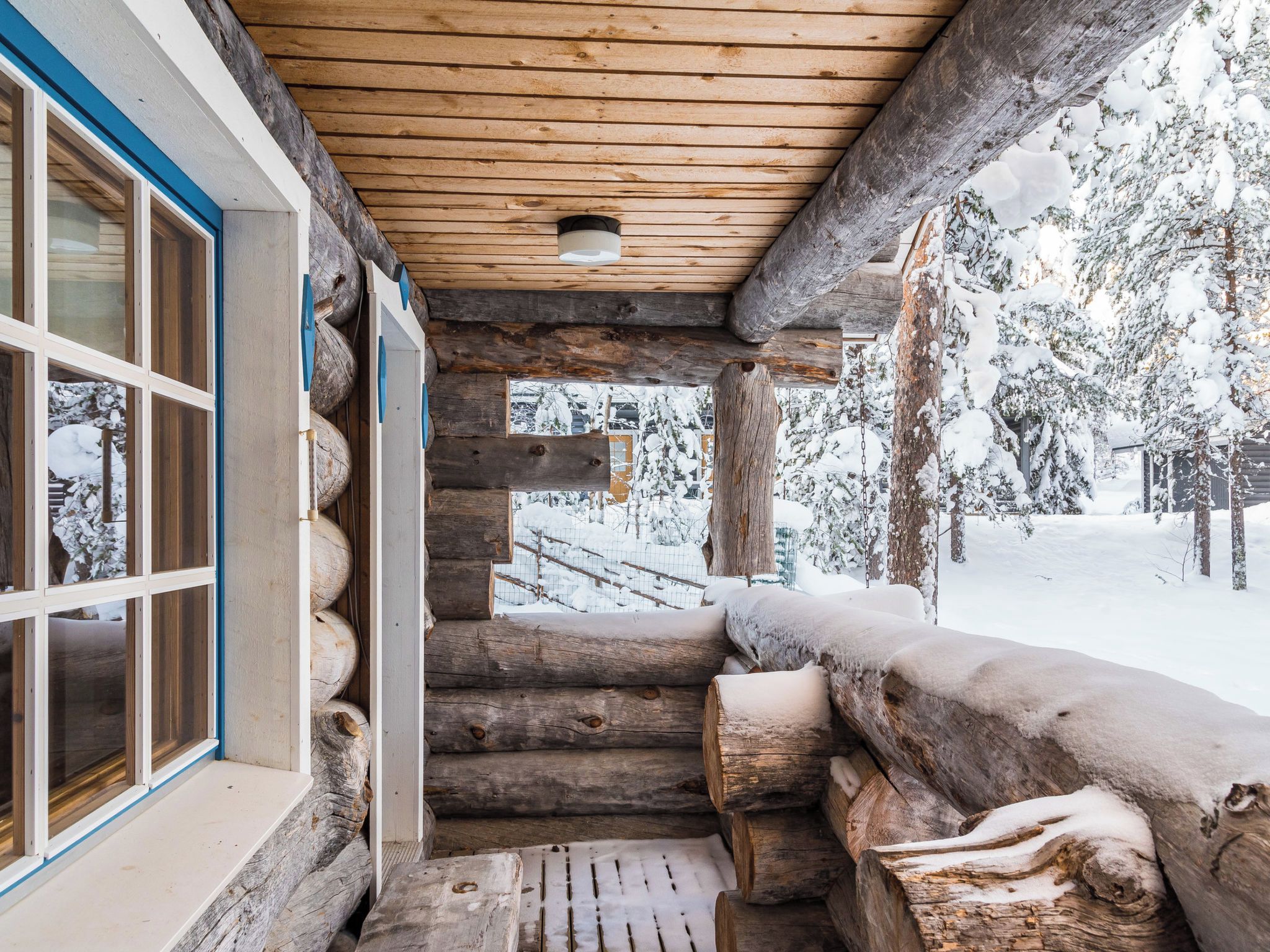 Une cabane en rondins avec un escalier en bois menant à une terrasse enneigée.