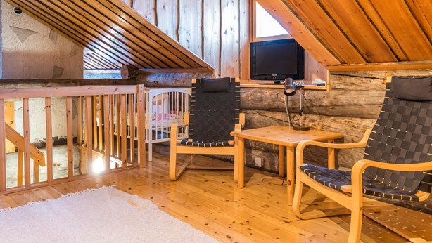 A cozy cabin interior with a wooden deck, a small table, two chairs, and a television on a wall.