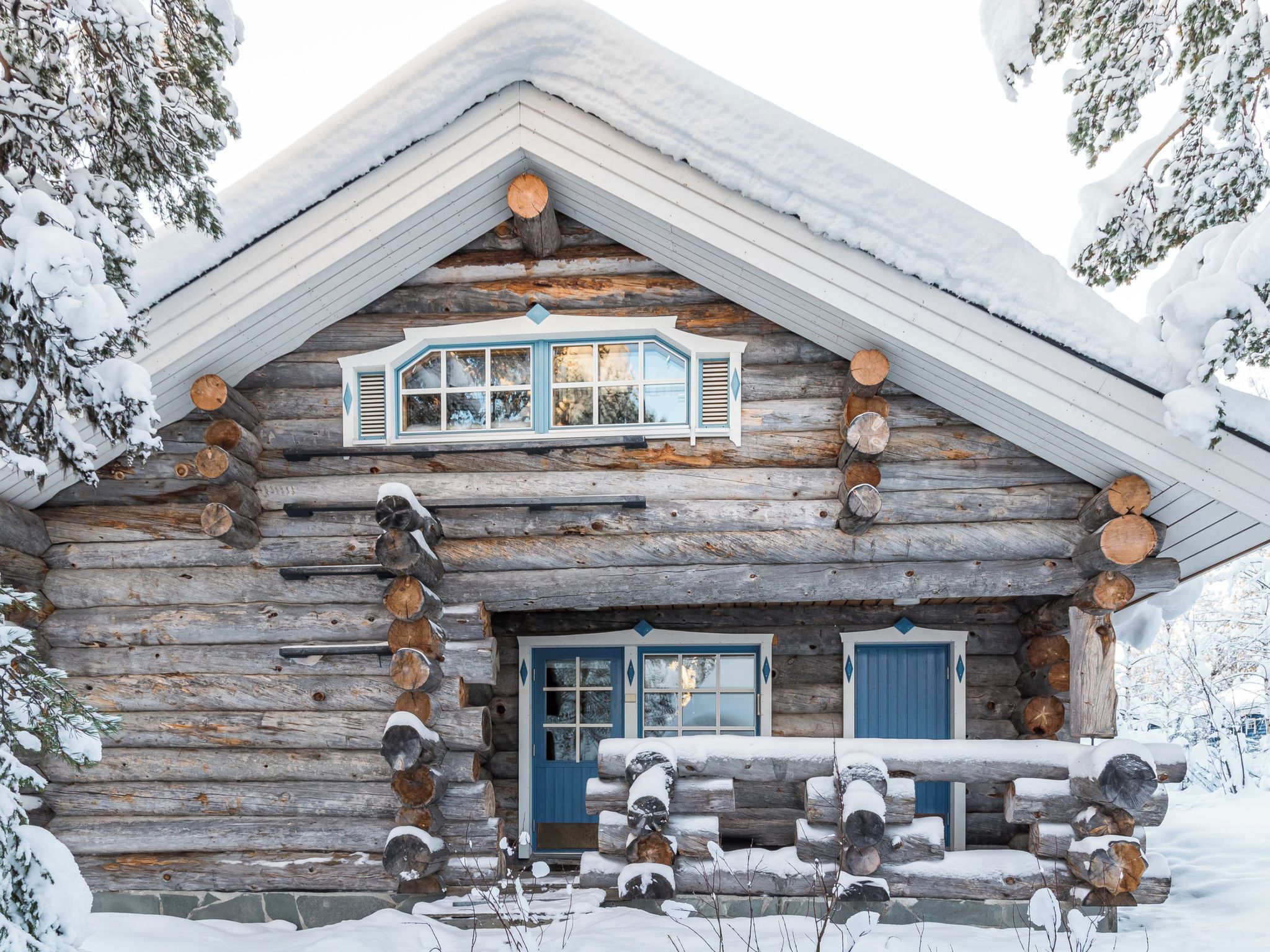 A log cabin with a gabled roof, a front porch with stacked logs, and a blue door.
