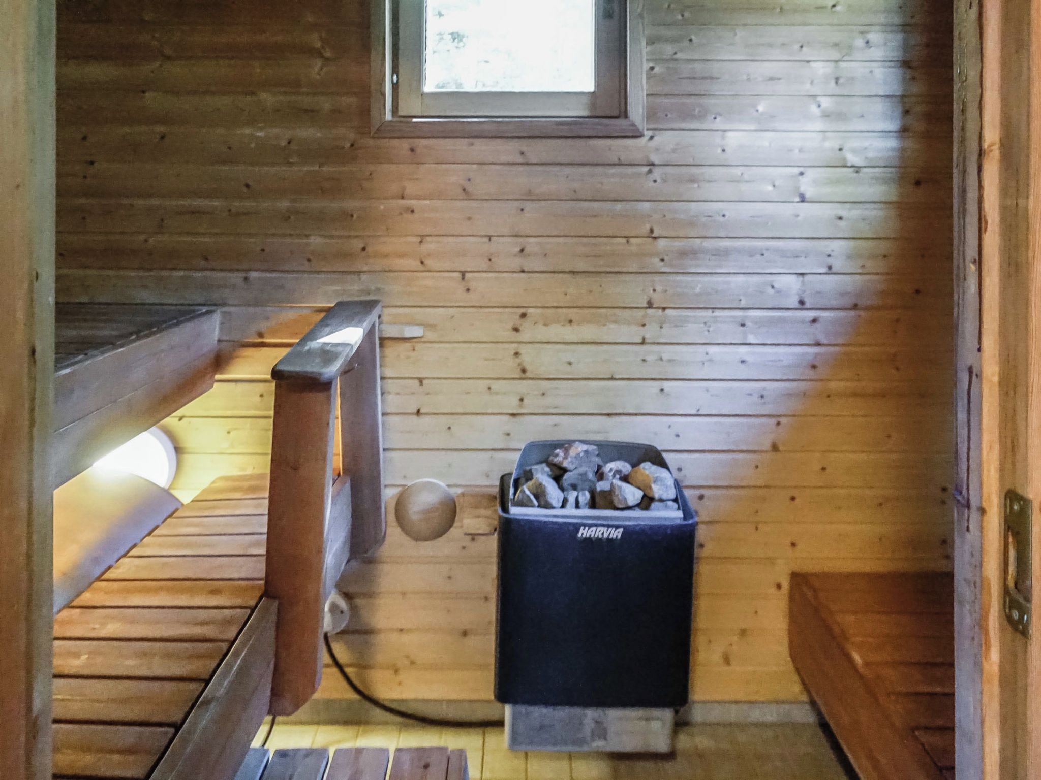 A wooden cabin interior with a bench, a small heater, and a trash bin labeled 'HARVIA'.