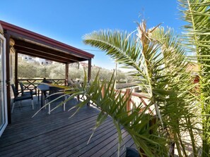 Una terraza de madera con mobiliario exterior, un espacio de estar cubierto y vistas del paisaje circundante.
