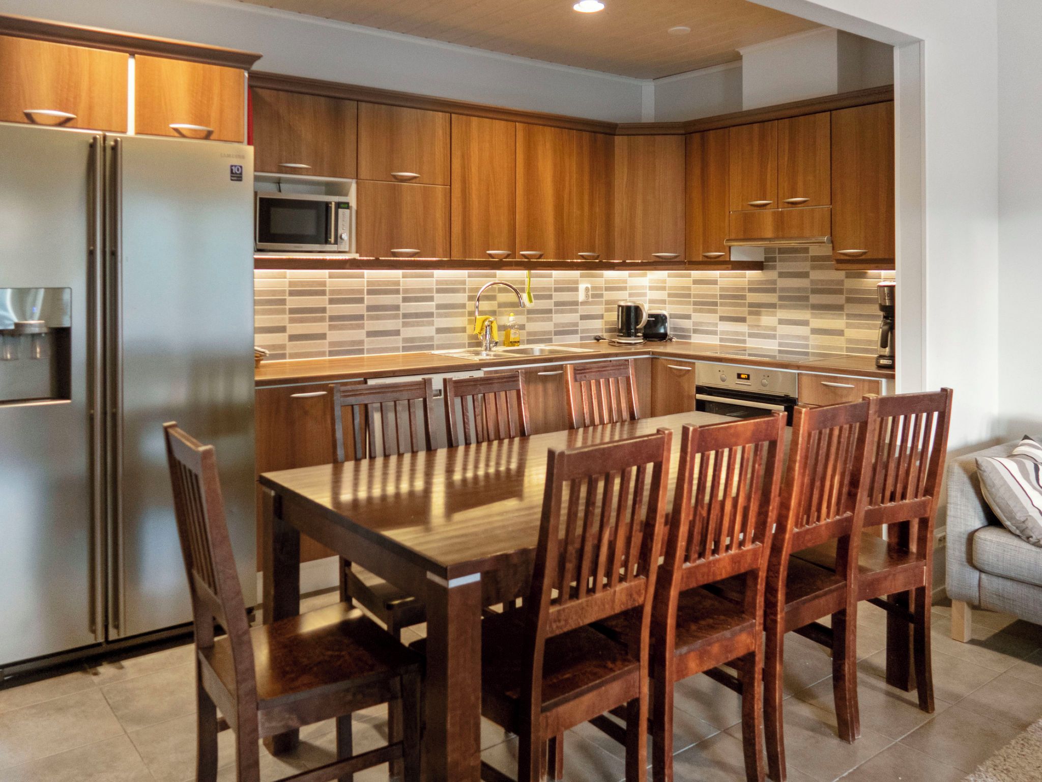 A modern kitchen with wooden cabinets, a stainless steel refrigerator, a microwave, and a dining area with wooden chairs and a table.