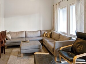 A living room with a grey sofa, a black leather chair, a wooden chair, and a remote control on the sofa. - 4 seasons a 2 by Interhome (Sotkamo)
