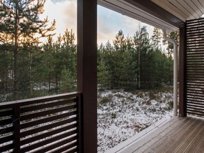 Una terraza de madera con vistas a zona boscosa cubierta de nieve.