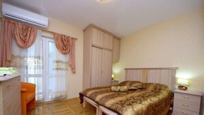 Une chambre à coucher comprenant un lit, une table de chevet, une commode, un fauteuil orange et un appareil de climatisation.