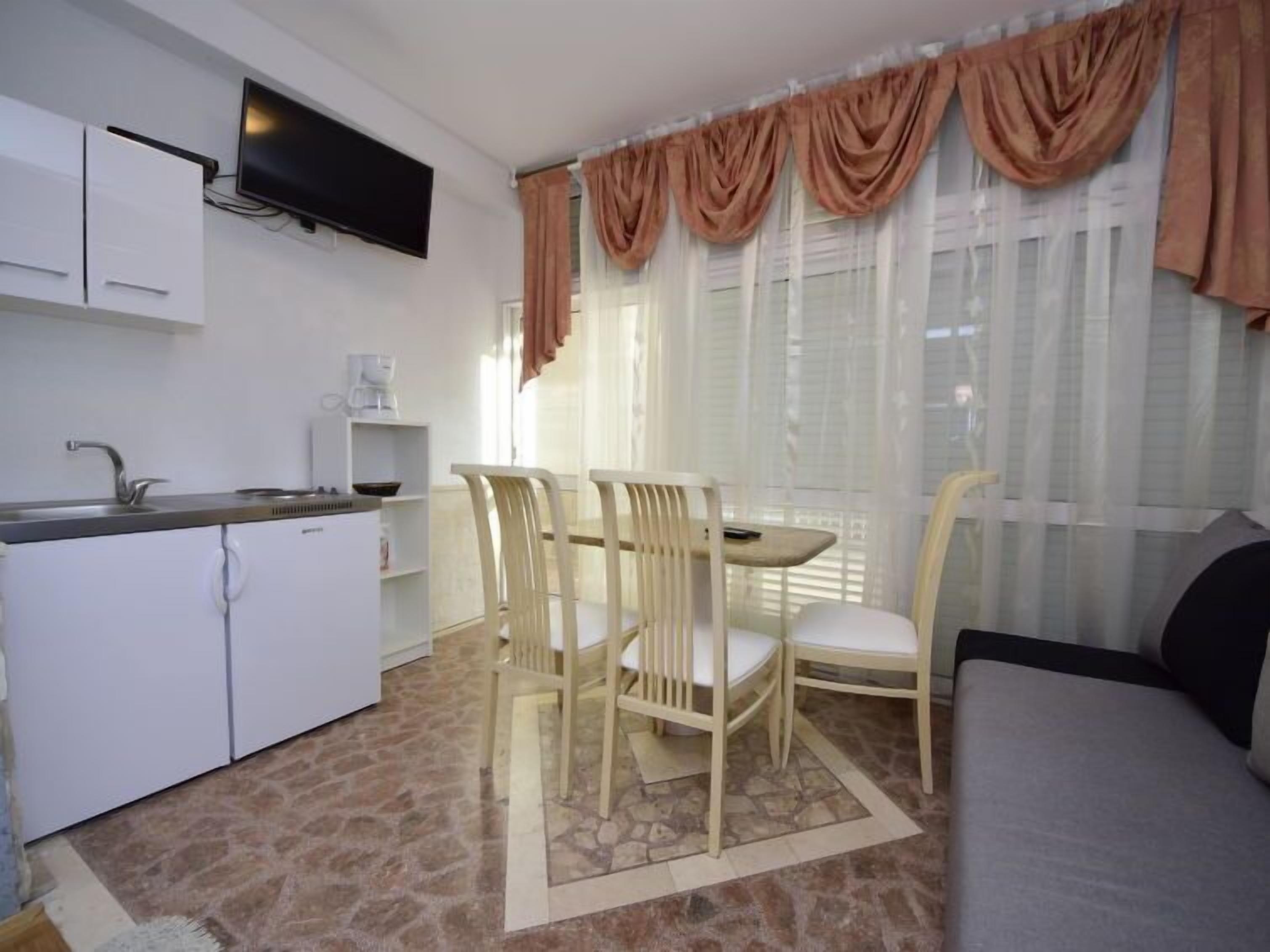 A compact kitchen with a dining area, a sofa, and a TV mounted on the wall.