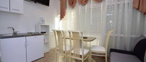 A compact kitchen with a dining area, a sofa, and a TV mounted on the wall.