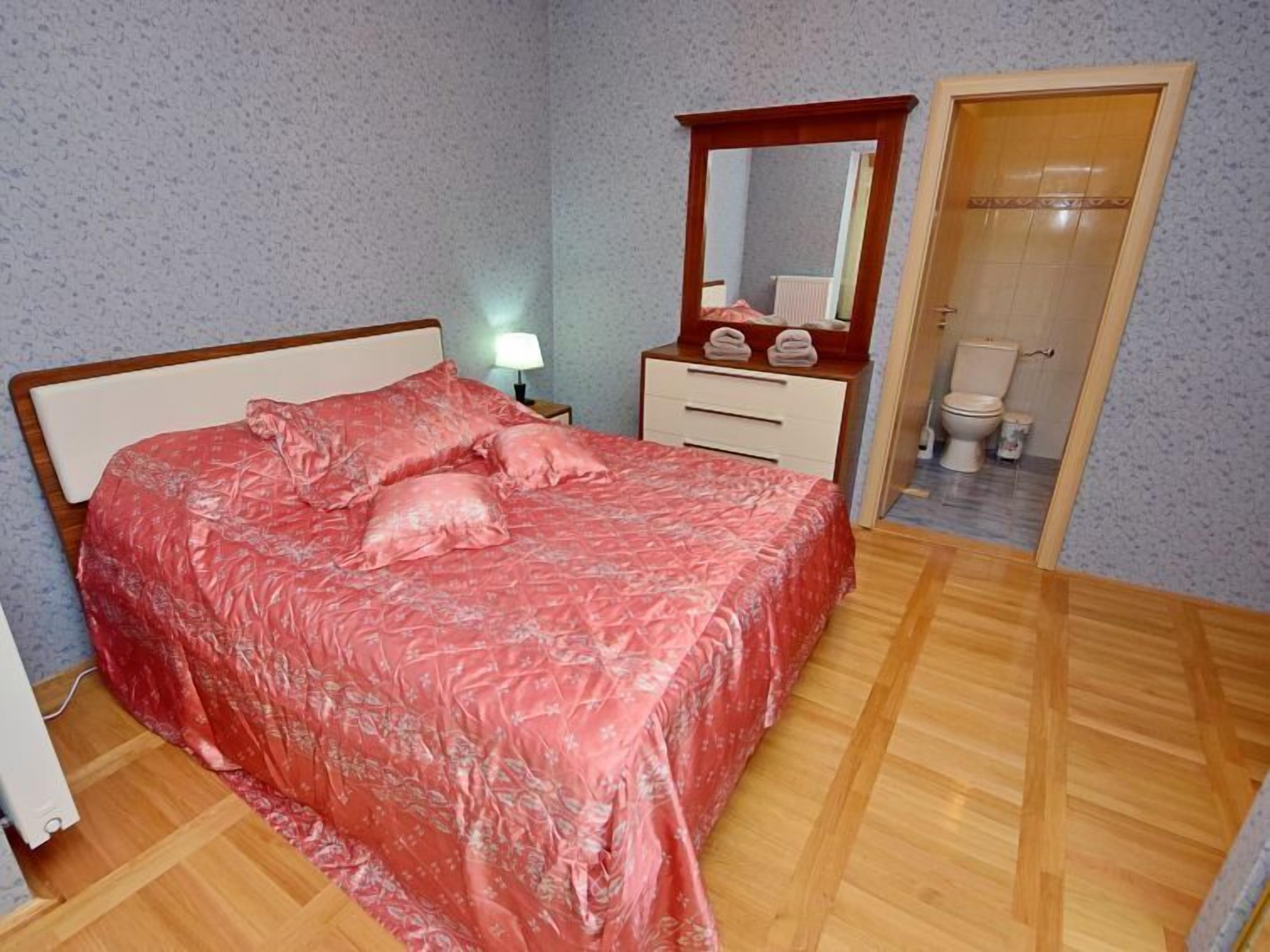 A bedroom with a bed, a nightstand, a dresser, a mirror, and a door leading to a bathroom.