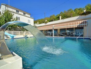 A swimming pool with a water feature, a covered seating area, and a building in the background. - Apartment Ojdana by Interhome (Zaton (Šibenik))