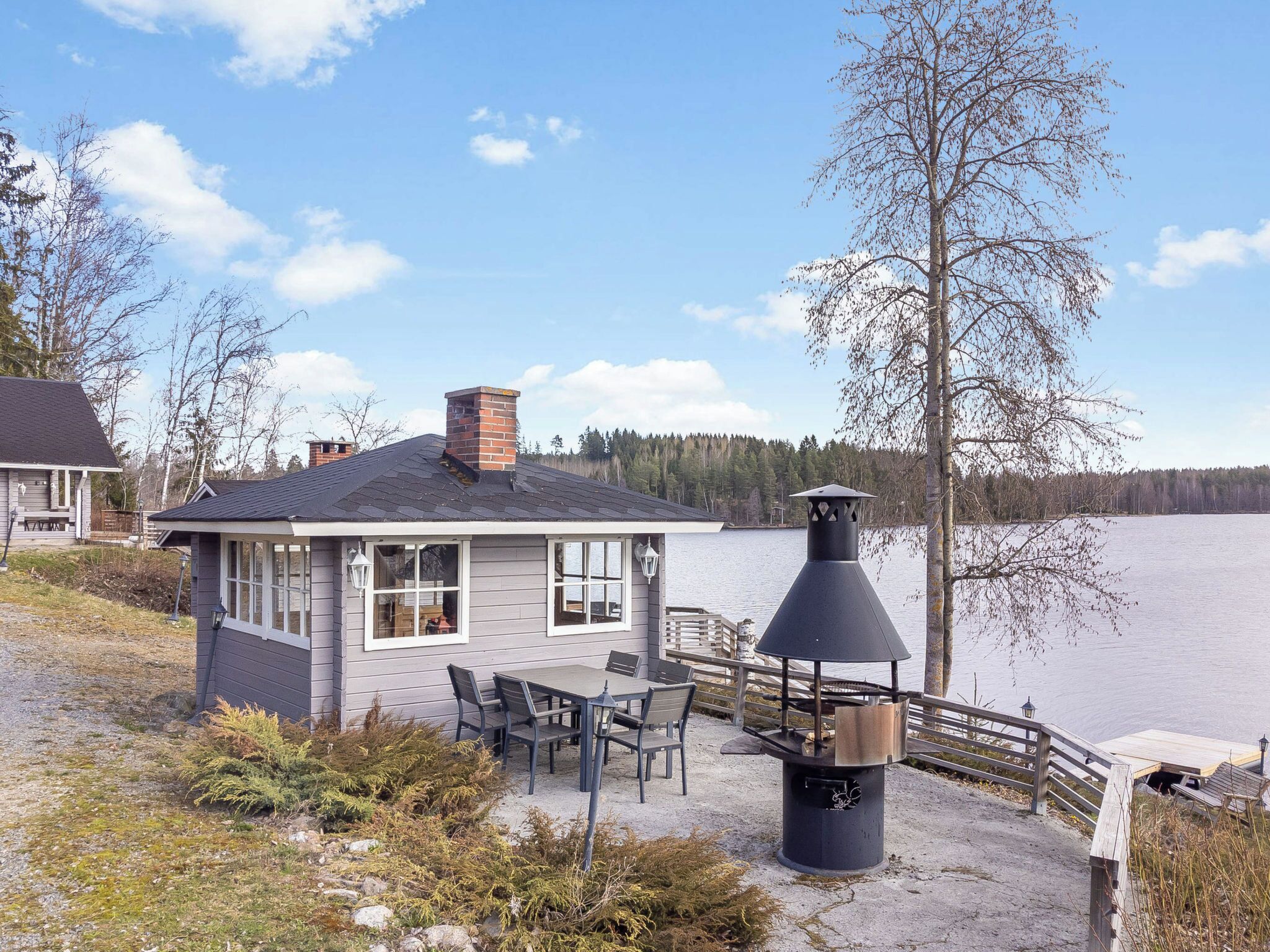 A lakeside cabin with a deck, outdoor seating, and a chimney.