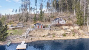Un chalet au bord du lac, avec un quai, un petit bateau et une colline boisée.
